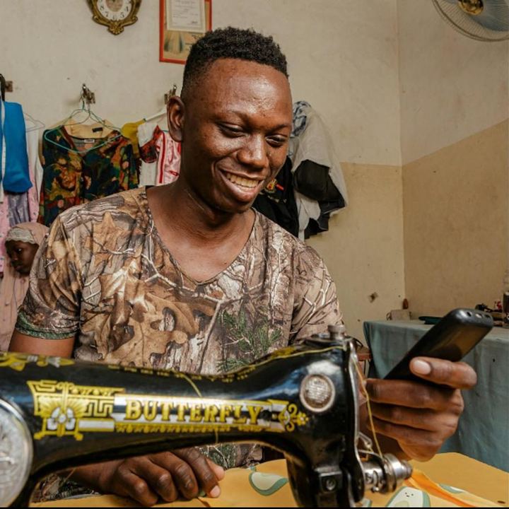 Un couturier souriant à sa machine, téléphone en main
